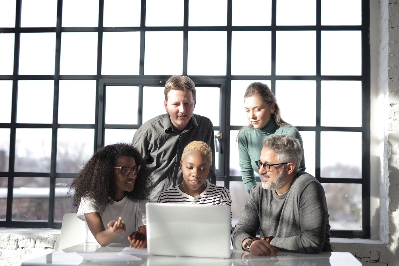 People sharing ideas around a laptop in a sunlit workspace
